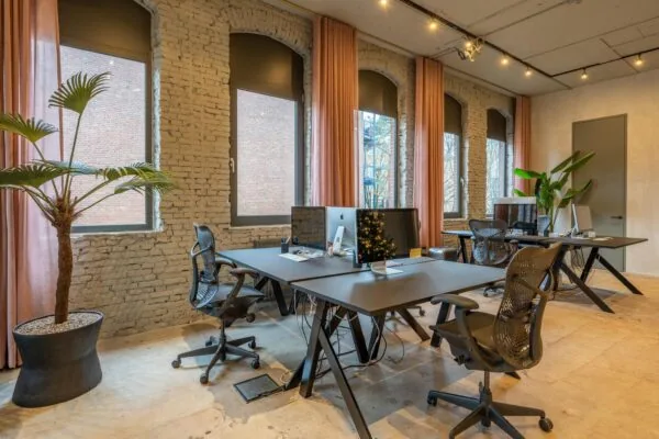 Modern ingerichte kantoorruimte aan de Admiraal de Ruijterweg met grote ramen, zwarte bureaus en designbureaustoelen.